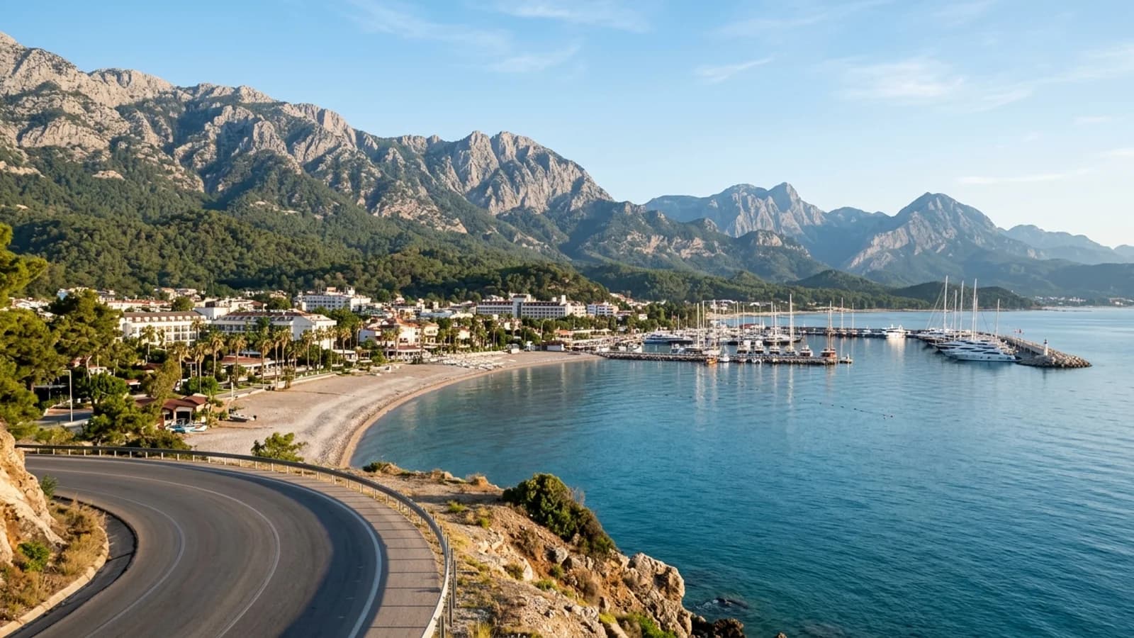 Een kiezelbaai in Kemer met een jachthaven en de met dennenbossen bedekte Beydaglari-bergen op de achtergrond.