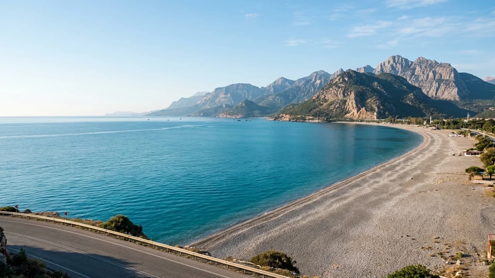 Ein langer grauer Kieselstrand in Konyaaltı an einer türkisfarbenen Bucht mit steilen Bergen im Hintergrund.