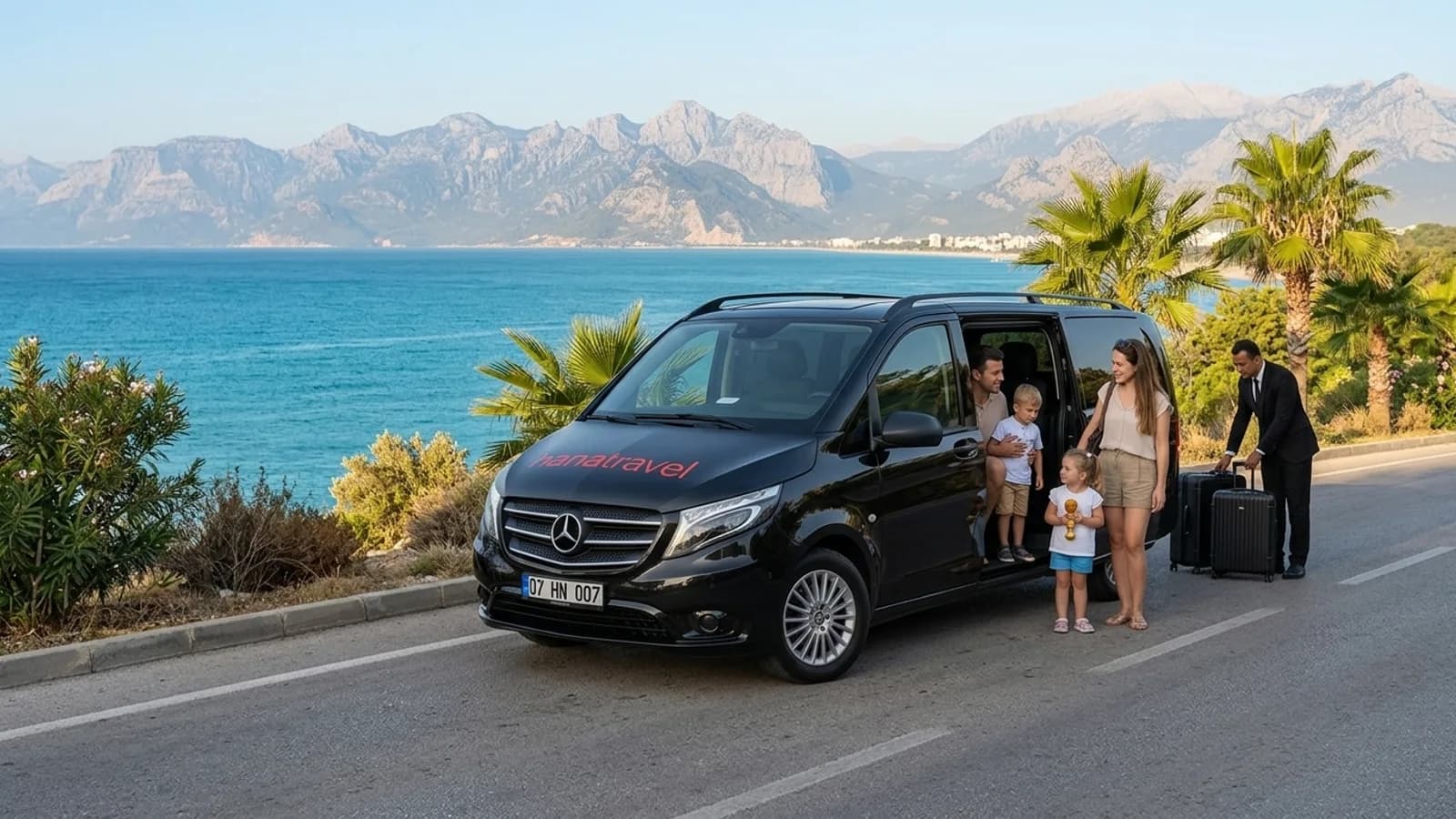A modern black transfer van driving along a scenic coastal road above the blue Mediterranean Sea.