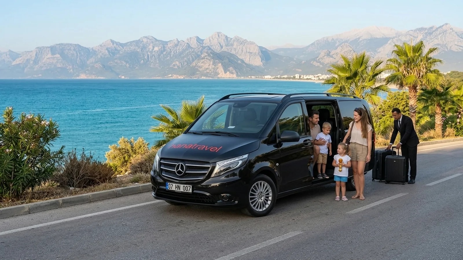 A modern black transfer van driving along a scenic coastal road above the blue Mediterranean Sea.